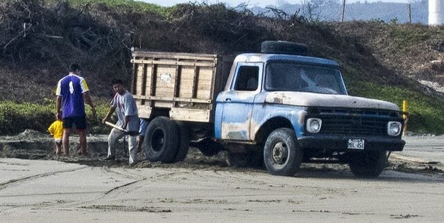Locals shoveling beach sand in truck for construction project